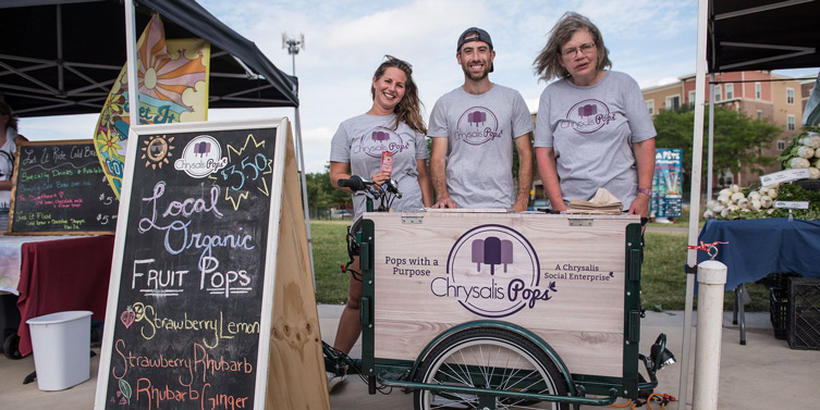 At a farmers market stand, Chrysalis Pops Manager Ashley, Previous Chrysalis Pops manager Max and
participant Barb standing next to the Chrysalis Pops Icicle Tricycle.